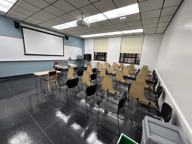 Front view of the classroom with a large whiteboard and projector screen.