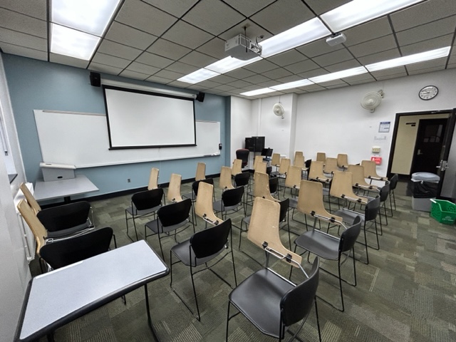 Front of the classroom with a white board and large projector screen.