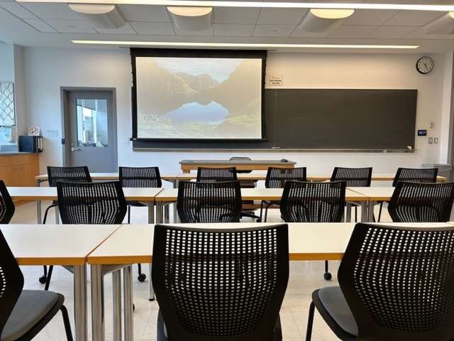 Front of the classroom with a large projector screen and blackboard.