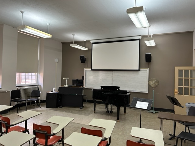 Front of the classroom with a large projector screen, whiteboard, and grand piano.