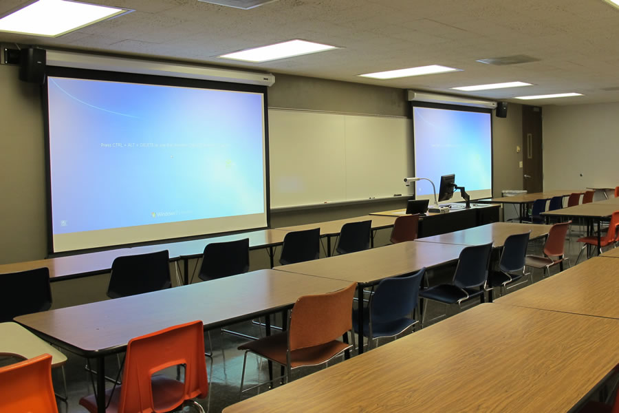 Front of the classroom with a large white board and two projector screens.