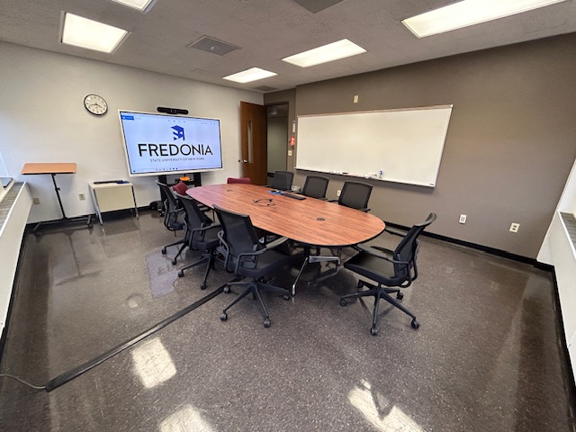 Front of the conference room with a large table, several chairs, and a whiteboard.