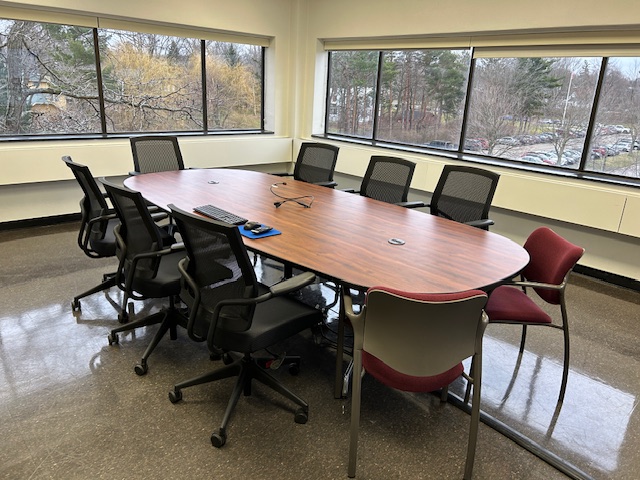 Back of the conference room with a large table, several chairs, and large windows on the back wall.