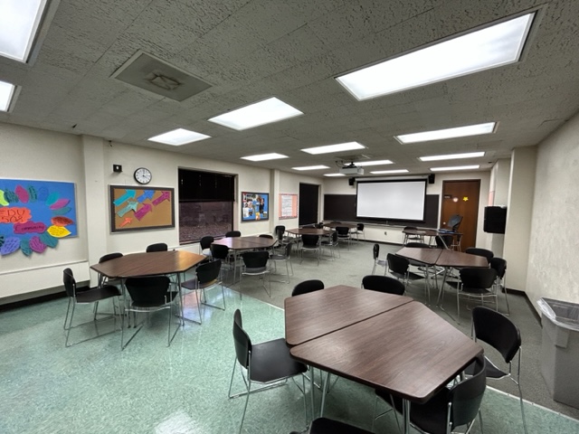 Front of the classroom with a large projector screen and black board.