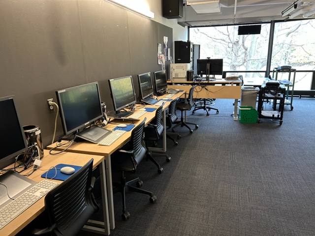 Student computer desks lined on the wall with large windows in the background.