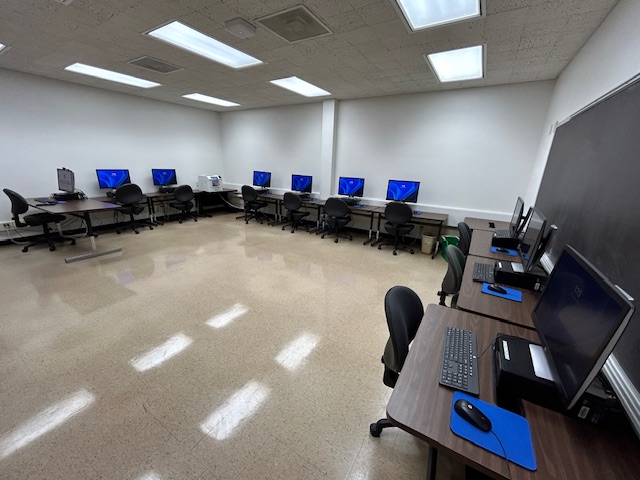 Back of the computer lab with several computer desks lined up on the walls.