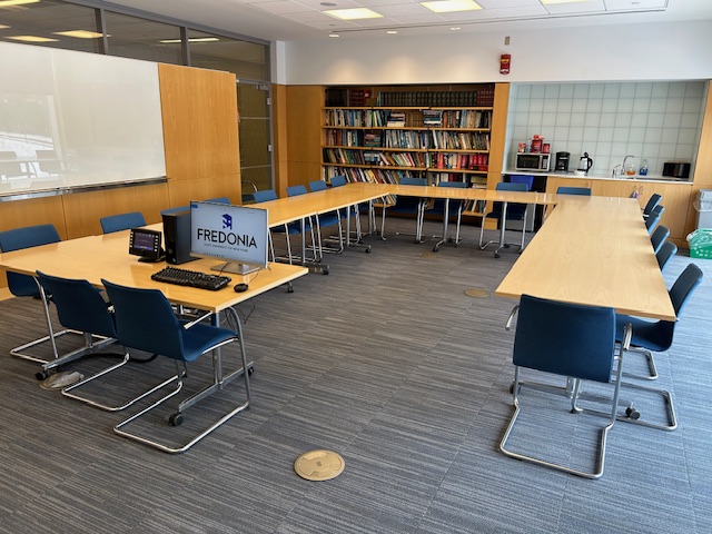 Back of the conference room with tables and chairs in a circle formation, and bookshelves on the back wall.