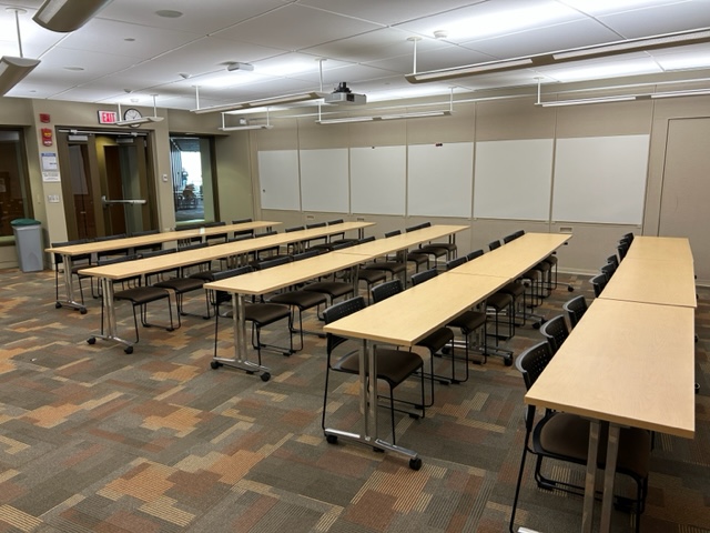 Back of the classroom with student desks arranged in rows and large windows on the back walls.