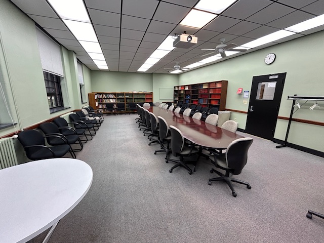 Back of the room with several bookshelves, and a conference table with several chairs around it and on the walls.