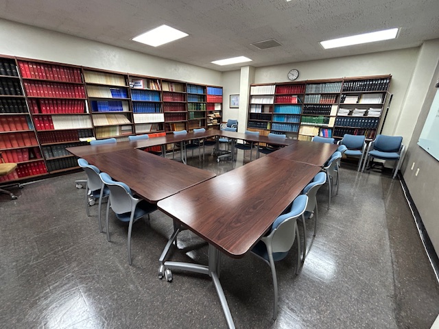 Back of the conference room with tables and chairs in a circle formation, and bookshelves on the back wall.