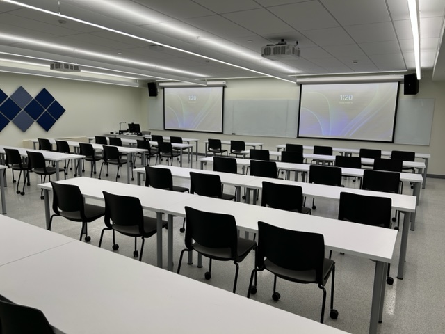Front of the classroom with a large whiteboard and projector screens.