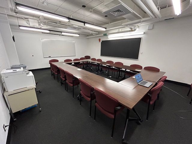 Back of the conference room with large tables and chairs and a large black board and whiteboard